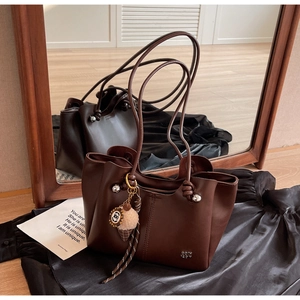 Detail of dark brown tote bag with long thin straps and plush ice cream pendant charm