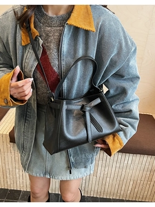 Detail of black leather tote bag featuring a decorative knot and dual handle design