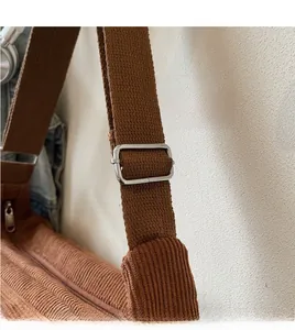 Detail of adjustable long shoulder strap and metal buckle on brown corduroy tote bag