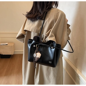 Detail of black leather tote bag with fluffy ice cream charm on beige trench coat