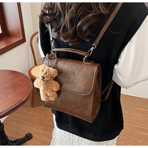 Dettaglio dello zaino vintage marrone con goffratura di lettere e ciondolo a forma di orso