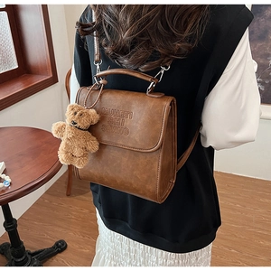 Dettaglio dello zaino vintage in pelle marrone con ciondolo a forma di orsetto di peluche