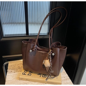 Detail of dark brown leather tote bag with knotted handles and ice cream charm on a desk