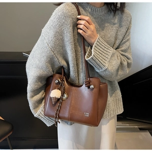 Close-up of brown leather tote bag with plush ice cream charm worn on a grey sweater