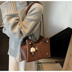 Detail view of brown shoulder bag with ice cream plush charm on casual outfit
