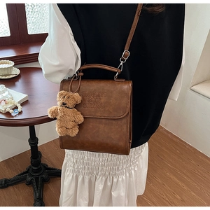 Detail view of brown vintage leather handbag with MUHETI text and plush bear charm