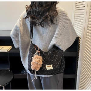 Détail du sac bandoulière noir en toile avec motifs cœurs et nœuds et breloque peluche