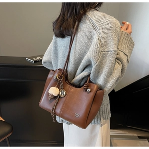 Detail of a brown tote bag featuring fine shoulder straps and a plush ice cream charm