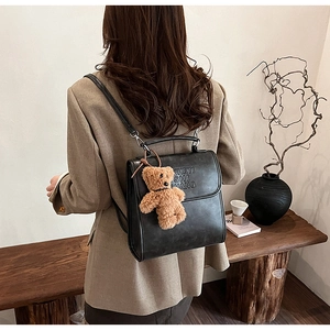 Dettaglio dello zaino vintage in pelle nera con lettere in rilievo e ciondolo a forma di orso