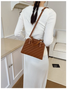 Bolso marrón con textura trenzada, correa ajustable y hebilla plateada sobre modelo