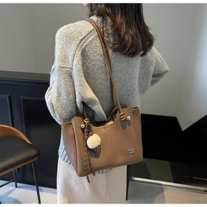 Detail of a brown leather tote bag showing knotted shoulder straps and plush charm