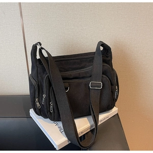 Detail of black corduroy tote bag featuring multi-zipper pockets and wide adjustable strap