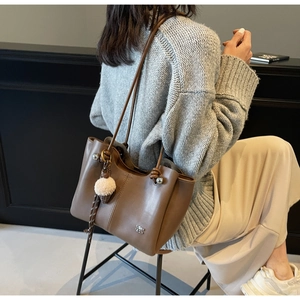 Detail of coffee brown leather tote bag with furry pendant and metallic rivet accents