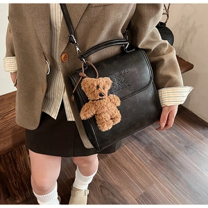 Close-up of vintage black crossbody bag featuring a brown plush bear and embossed text