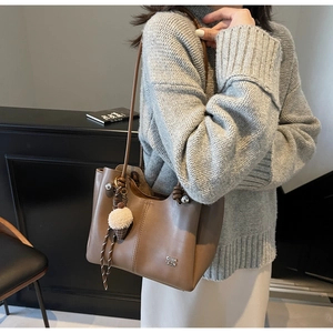 Detail of coffee brown leather tote bag with vertical stitching and cute charm