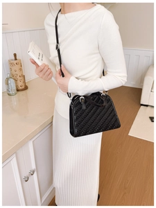 Detalle del bolso tote negro con textura de tejido diagonal y hebillas plateadas en modelo