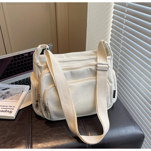 Detail of off-white corduroy tote bag featuring multi-zipper pockets and wide shoulder strap