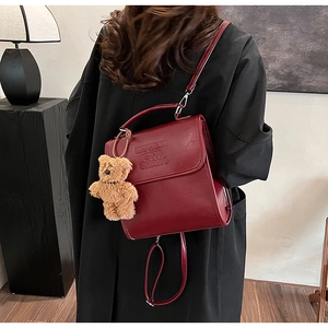 Detail of burgundy leather handbag with embossed letters and a brown plush bear charm