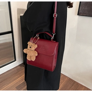 Dettaglio della borsa in pelle rosso scuro con ciondolo orsetto e logo in rilievo