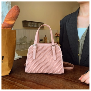 Detalle de bolso bandolera rosa de piel sintética con patrón tejido y hebilla de plata