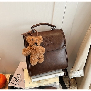 Detail of dark brown vintage faux leather backpack with plush bear charm and embossed logo