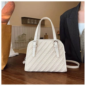 Detalle de bolso acolchado blanco crema con textura ondulada sobre madera oscura