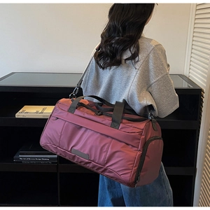 Model carrying a burgundy waterproof nylon travel bag with shoe compartment and side pockets