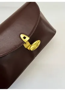 Detailed view of dark brown leather handbag with custom gold hardware buckle and secure lock