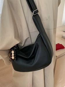 Minimalist black leather hobo bag with bead tassel and silver buckle on a trench coat model