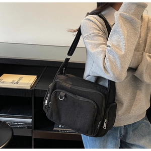 Detail of black corduroy tote bag featuring multi-zipper pockets and adjustable strap