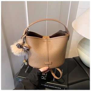 Detail of khaki lychee grain leather bucket bag with plush pom-pom and leopard bow charm
