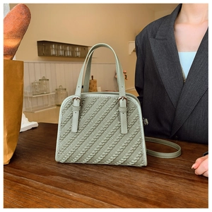 Detalle de bolso bandolera verde claro con textura trenzada y elegantes cierres metálicos