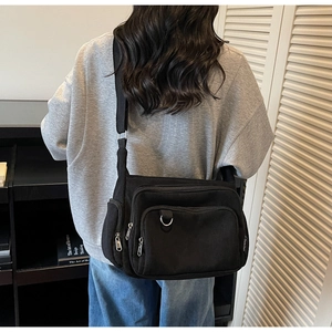 Detail of black corduroy crossbody bag texture and silver zippers on a wide shoulder strap