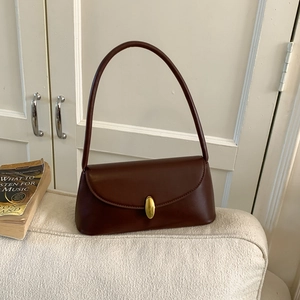 Close-up of a vintage brown leather underarm bag with an oval gold buckle on a sofa