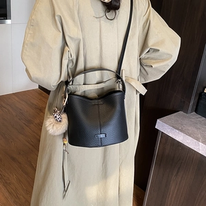 Detail of black lychee texture bucket bag with leopard bow plush charm on khaki trench coat