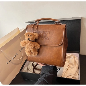 Dettaglio dello zaino vintage marrone con lettere a rilievo e ciondolo a forma di orso