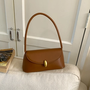 Detail of caramel leather shoulder bag with gold oval buckle on a white sofa