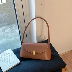 Detail of caramel leather shoulder bag with gold clasp and vintage book on black seat