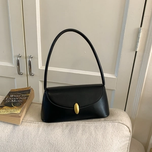 Detail of minimalist black underarm bag with gold oval magnetic clasp on a white sofa