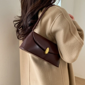Detail of a dark brown vintage leather baguette bag with a gold buckle on wool coat