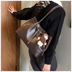 Detail of dark brown tote bag with leather texture and cute plush bear accessory