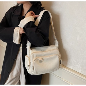 Detail of white corduroy tote bag featuring multiple zip pockets and silver D-ring buckle