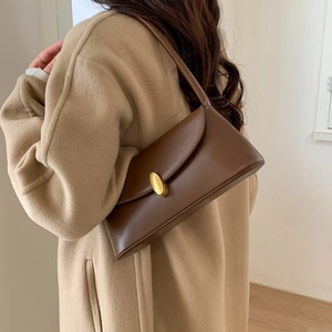 Detail of vintage dark brown leather shoulder bag with oval gold buckle on a wool coat