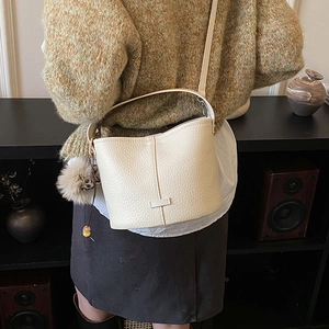 Detail of a beige pebbled leather bucket bag with fur ball charm and beaded pendant