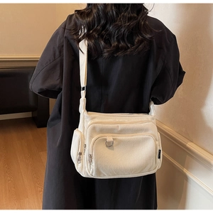 Detail of off-white corduroy crossbody bag showing zipper pockets and ribbed texture