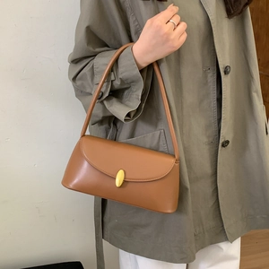 Detail of a brown leather shoulder bag with a gold oval clasp worn with a trench coat