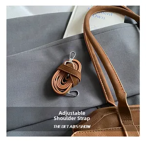 Détail de la bandoulière réglable du sac Boston en cuir brun avec crochets argentés