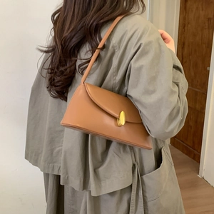 Detail of a brown leather baguette shoulder bag with a gold metal lock on a green coat
