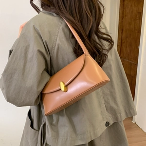 Close-up of caramel leather underarm bag featuring a gold oval clasp and sleek finish