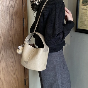 Detail of beige pebble leather bucket bag featuring a leopard print pom-pom and strap
